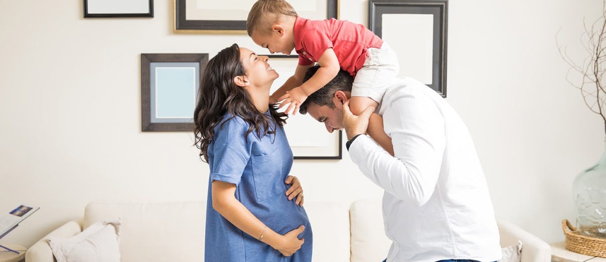 Cheerful expectant couple playing with son in living room at home