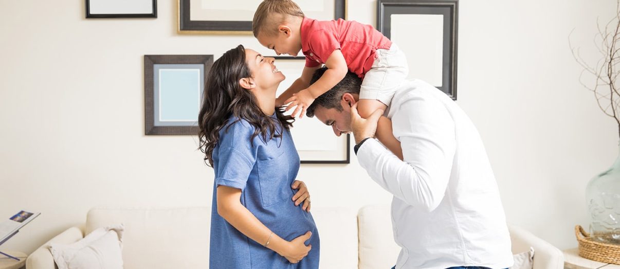 Cheerful expectant couple playing with son in living room at home