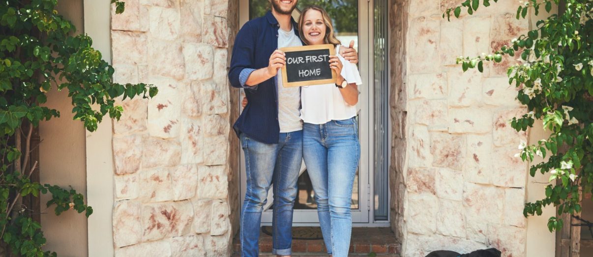 Portrait of a young couple holding a chalkboard with "our first home" written on it