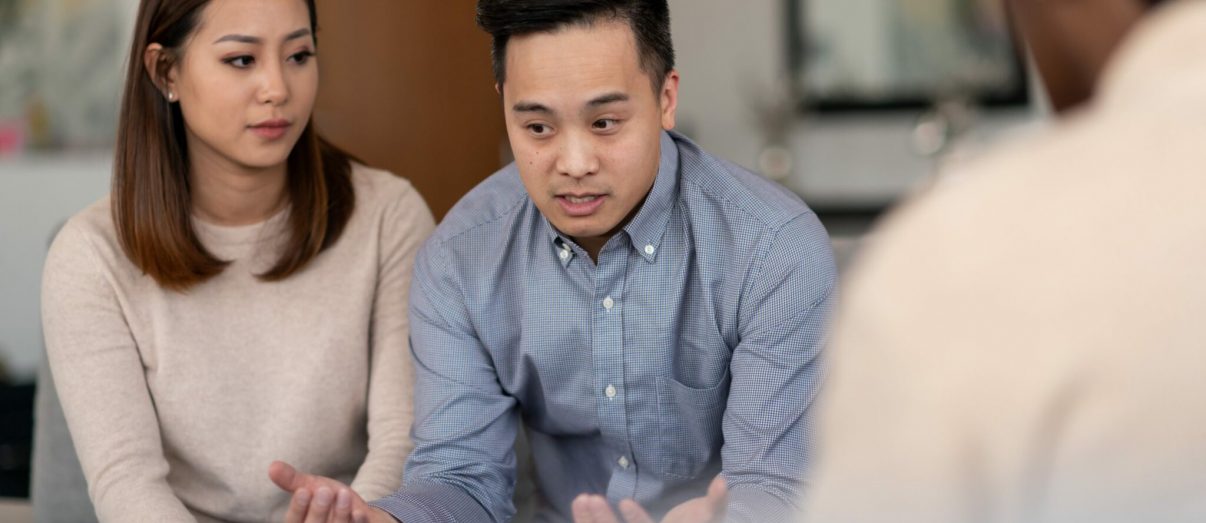 An Asian married couple talks to a therapist together about their life. They are attentive and focused on making their marriage work.