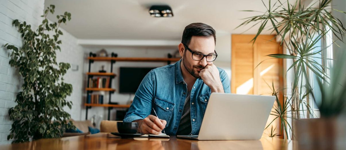 Serious man looking at laptop and taking notes in notebook, portrait.