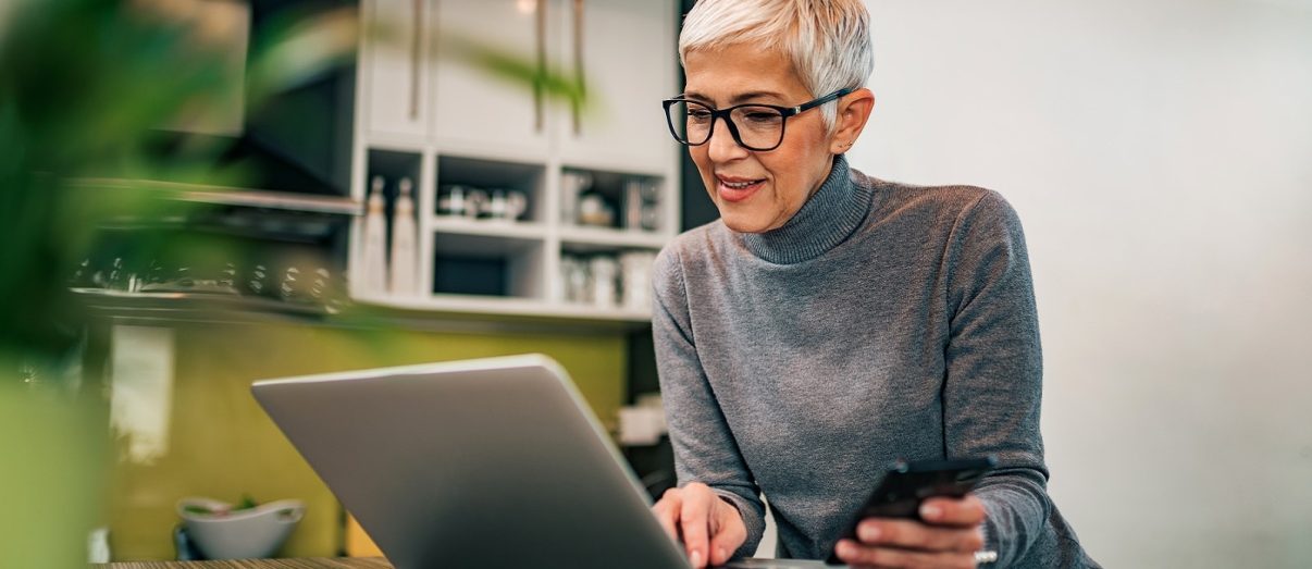 Modern mature woman using laptop and smart phone at home, portrait.