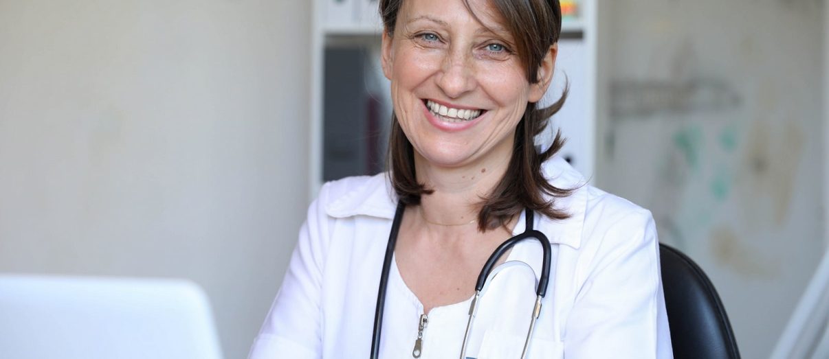 Confident female doctor posing in her office and smiling at camera