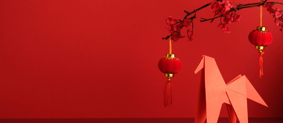 Chinese New Year setup with an origami paper horse, red lantern, and plum blossom branch against a bright red background. Ideal for Year of the Horse and Asian greeting card design