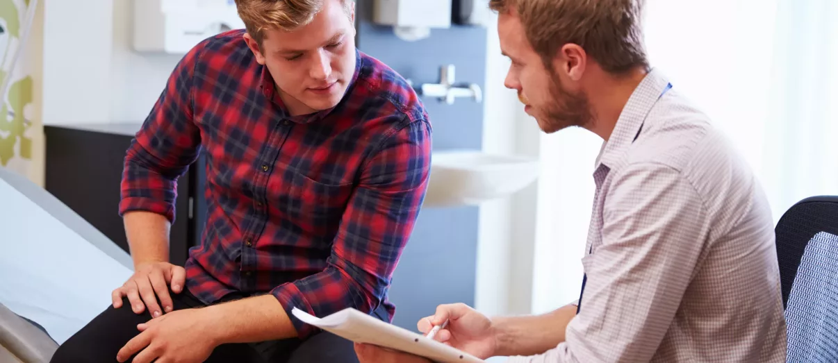 Male Patient And Doctor Have Consultation In Hospital Room