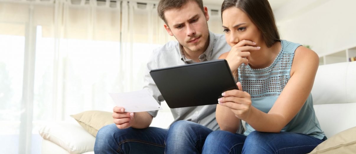 Worried couple checking bank account trouble online in a tablet sitting on a couch in the living room at home