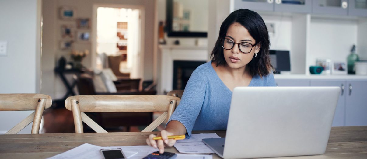 Shot of a young woman using a laptop and calculator while working from home